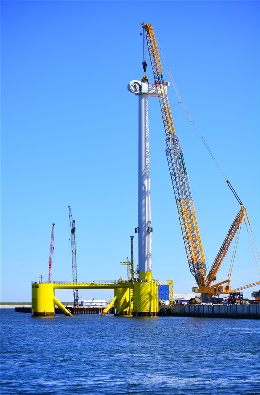 A landside crawler crane lifting a nacelle onto a floating substructure.